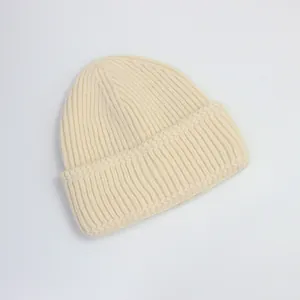 Gros plan détaillé montrant la texture en maille côtelée et le large revers du bonnet beige