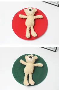 Detail von roten und dunkelgrünen Wollbaretts mit einem Plüsch-Teddybären-Dekor