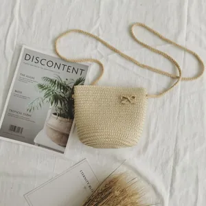 Dettaglio della borsa a secchiello in paglia beige con fibbia a fiocco dorata su tessuto