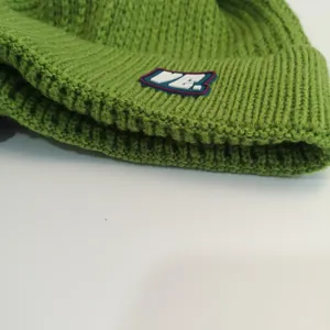 Close-up of cable knit grass green beanie featuring thick ribbed texture and VE. logo patch