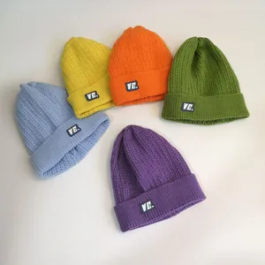 Detail of multi-color thick knit beanies with cable patterns and VE label logo