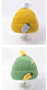 Detail von flauschigen Baby-Strickmützen mit Hasenohren und Karottenmuster in Grün und Gelb