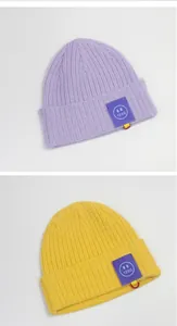Details der Stricktextur und Smiley-Aufnäher auf gelben und lila Mützen