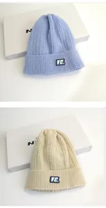 Dettaglio di berretti in maglia a trecce blu chiaro e crema con patch ricamata VE