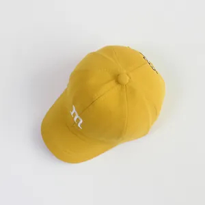 Detail van gele katoenen kinderpet met wit m-borduurwerk en een gebogen klep