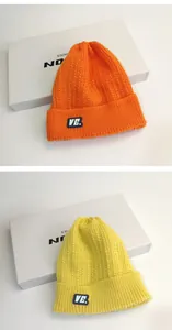 Dettaglio di berretti in maglia a trecce arancione e giallo con etichetta VE