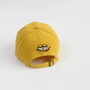 Detail van een gele katoenen honkbalpet met metalen gesp en smiley-borduurwerk op de rug