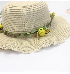 Dettaglio di un cappello di paglia beige con tesa a onde e fascia decorativa con api e foglie
