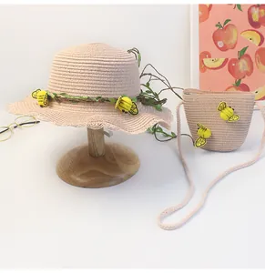 Dettaglio cappello di paglia rosa e borsa a tracolla con decorazioni di api e viti