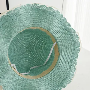 Detail of mint green straw hat showing scalloped brim and elastic chin strap