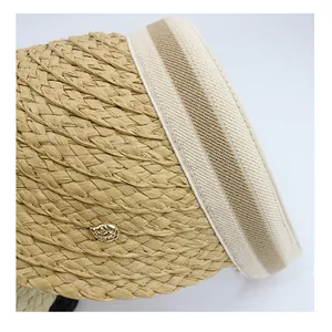 Detail of woven straw sun hat with striped ribbon edge and golden leaf emblem