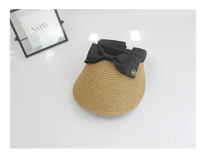 Detail of beige straw sun visor with black bow and gold M metal charm on white desk