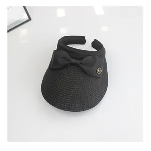 Detail of black woven visor hat with elegant bow and golden M-logo metallic badge