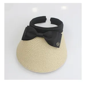 Detailed close-up of woven straw sun hat with black ribbon bow and metal M emblem