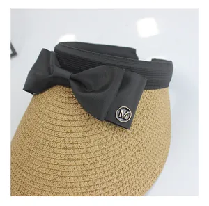 Close-up of straw sun hat featuring a black ribbon bow and gold metal 'M' logo detail