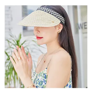 Detail of straw sun visor with checkerboard band and gold logo on female model