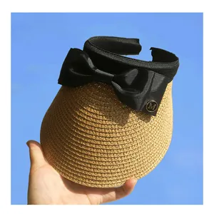 Detail of straw sun visor with large black satin bow and golden metal M letter logo