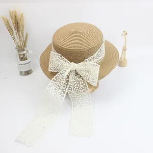 Detailed top view of a flat top straw hat featuring a cream lace ribbon bow and tassels