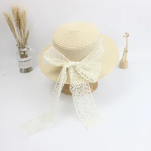 Detail of cream straw hat featuring wide floral lace ribbon and oversized bow decoration
