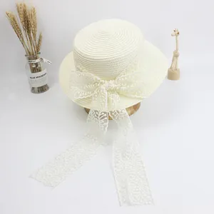 Close-up of cream straw hat featuring a large lace bow and elegant floral embroidery