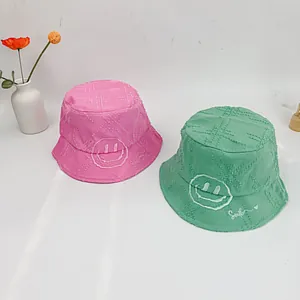 Detail of frayed edge cotton bucket hats with smile embroidery and cross texture