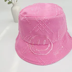 Detailed macro of pink cotton bucket hat featuring smiley face embroidery and distressed texture