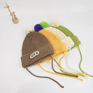 Detailed knit texture of baby pom-pom hats in various colors with windproof chin straps