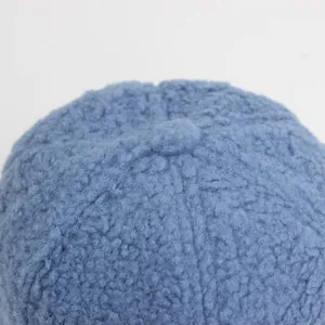 Nahaufnahme der hellblauen Lammwolle-Textur und des oberen Knopfdetails einer Wintermütze