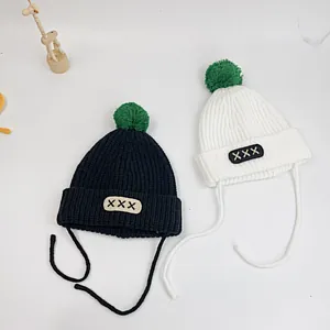 Detail of knitted baby hats with green pom poms and side ties for secure fitting