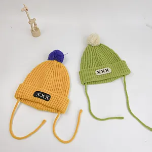 Flat lay of knit beanies with colorful pom-poms and letter patches for toddlers