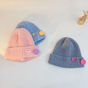 Close-up of knit hats showing soft vertical rib textures and colorful smiley face pin details