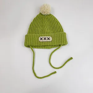 Detail view of green knitted baby hat featuring a soft pom-pom and adjustable chin straps