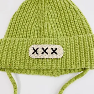 Macro detail of grass green knit baby hat with ribbed texture and embroidered XXX patch