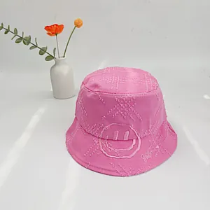 Detailed view of pink cotton bucket hat with frayed edges and smiley face embroidery