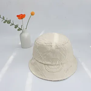 Detail of beige cotton bucket hat featuring fringe embroidery and a yellow smiley face