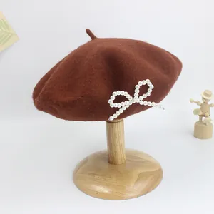 Detail einer dunkelbraunen Wollbaskenmütze mit einer weißen Perlschleife auf Holzständer