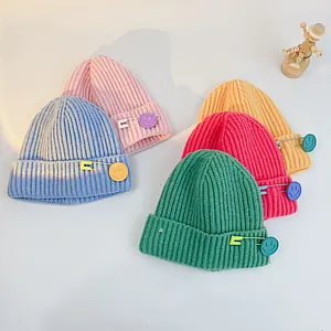 Flat lay of colorful ribbed knit beanies for children with cute smiley pin detail