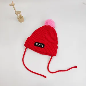 Detail of red knit baby hat with pink pom-pom, cross-stitch patch and earflaps