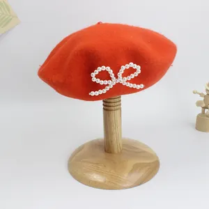 Detail der roten Wollbaskenmütze mit weißer Perlen-Schleife auf einem Holzständer