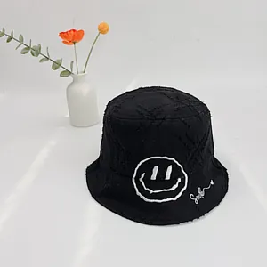 Detailed close-up of a black canvas fisherman hat featuring smile embroidery and frayed edges