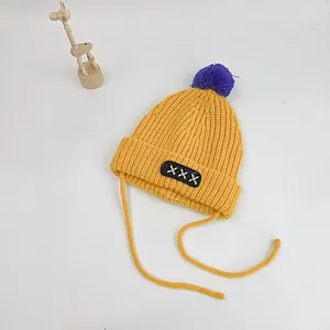 Detailed close-up of yellow knit baby hat with purple pompom and soft chin straps