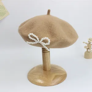 Detail der Wollbaskenmütze in Khaki mit elegantem weißen Perlenbogen auf einem Holzständer