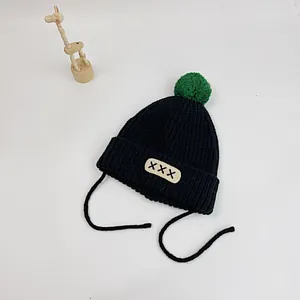 Close-up of black ribbed knit baby hat with green pompom and beige patch detail