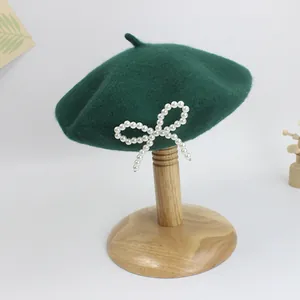 Detail von dunkelgrüner Wollbaskenmütze mit Schleife aus weißen Perlen an der Seite