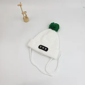 Detail of white knit baby hat with green pom-pom and secure chin straps for winter