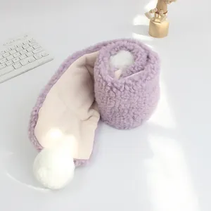 Dettaglio della sciarpa viola in lana di agnello con morbida texture e pompon bianchi