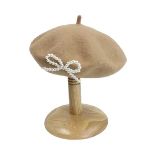 Khaki-Wollbaskenmütze mit elegantem Perlenbogen-Dekor auf einem Holzständer präsentiert