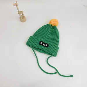 Detail of green knit baby hat with yellow pom-pom and embroidered patch strap