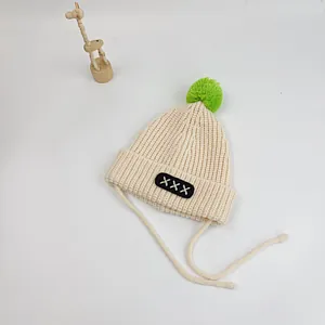 Close-up of baby knit hat with large green pompom and embroidered patch details
