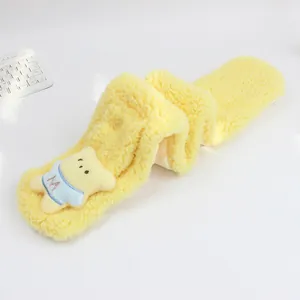 Détail d'une écharpe en peluche jaune avec ornement d'ours et design croisé pour enfants